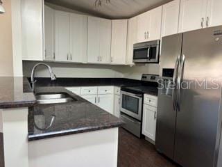 kitchen with appliances with stainless steel finishes, a sink, dark stone countertops, a peninsula, and white cabinetry
