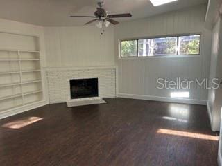 unfurnished living room featuring a brick fireplace, wood finished floors, baseboards, ceiling fan, and built in shelves
