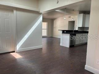 kitchen featuring dark countertops, baseboards, stainless steel dishwasher, and dark wood-style floors