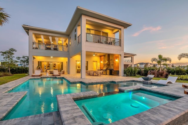 7905 Jacks Club Dr, Kissimmee, FL 34747 - back of property at dusk featuring a balcony, a patio, stucco siding, and a pool with connected hot tub