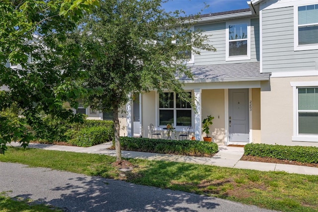 townhome / multi-family property with a porch, stucco siding, and roof with shingles