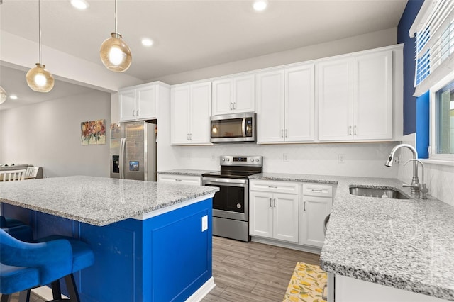 kitchen with stainless steel appliances, a sink, a kitchen bar, light wood-style floors, and a kitchen island