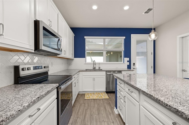 kitchen featuring appliances with stainless steel finishes, a sink, light wood-style floors, white cabinetry, and backsplash