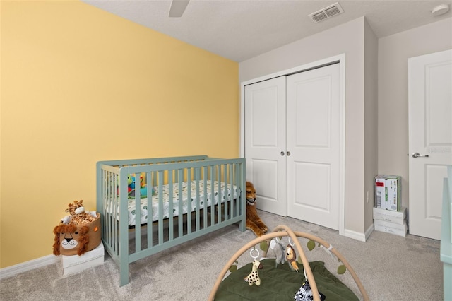 bedroom featuring carpet, a closet, baseboards, a crib, and a ceiling fan