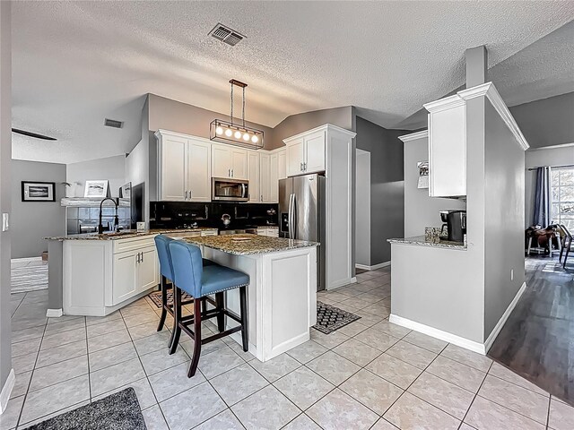 kitchen with light stone countertops, stainless steel appliances, a peninsula, light tile patterned floors, and visible vents