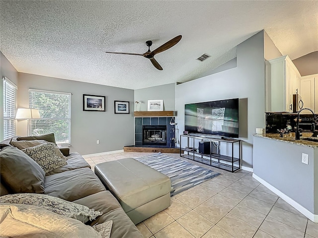 living area featuring a fireplace, a textured ceiling, a ceiling fan, light tile patterned floors, and visible vents