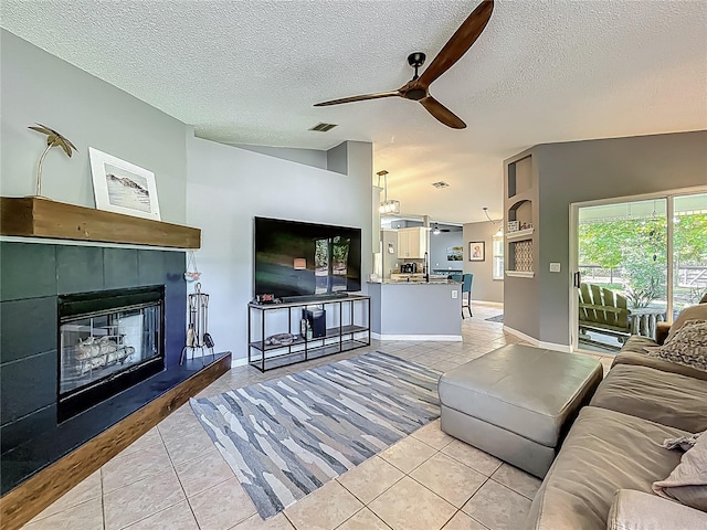 living area featuring visible vents, light tile patterned flooring, a fireplace, ceiling fan, and a textured ceiling