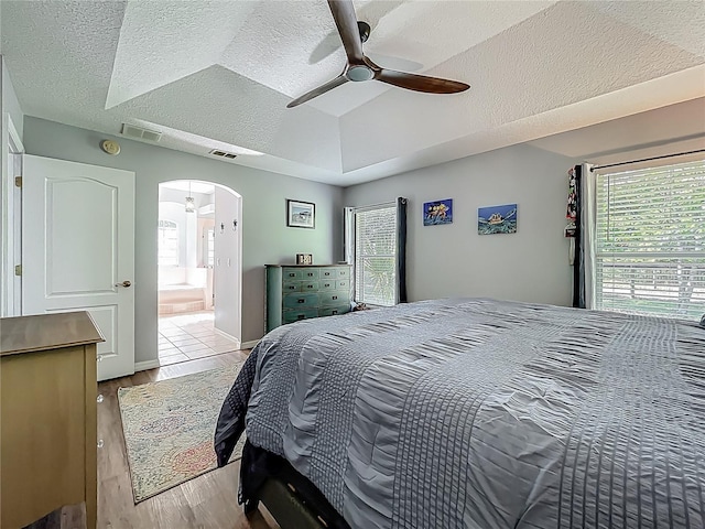 bedroom featuring visible vents, arched walkways, light wood-style flooring, and a textured ceiling