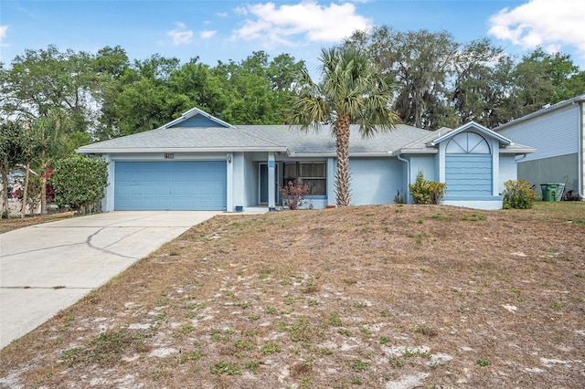 ranch-style home with concrete driveway, an attached garage, a shingled roof, and stucco siding