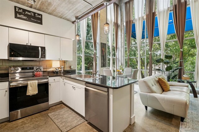 kitchen with dark countertops, white cabinetry, tasteful backsplash, a sink, and appliances with stainless steel finishes