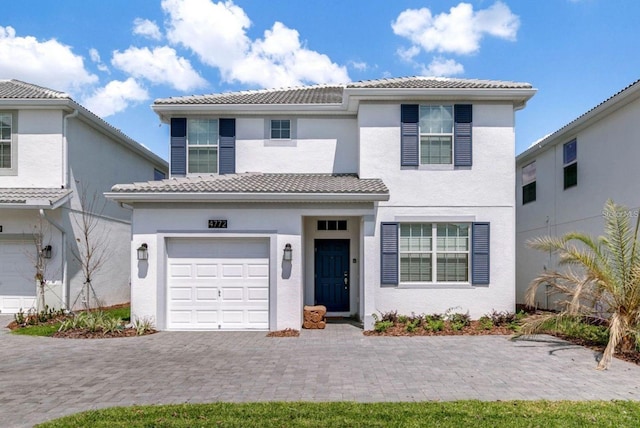 mediterranean / spanish home featuring a tiled roof, an attached garage, decorative driveway, and stucco siding