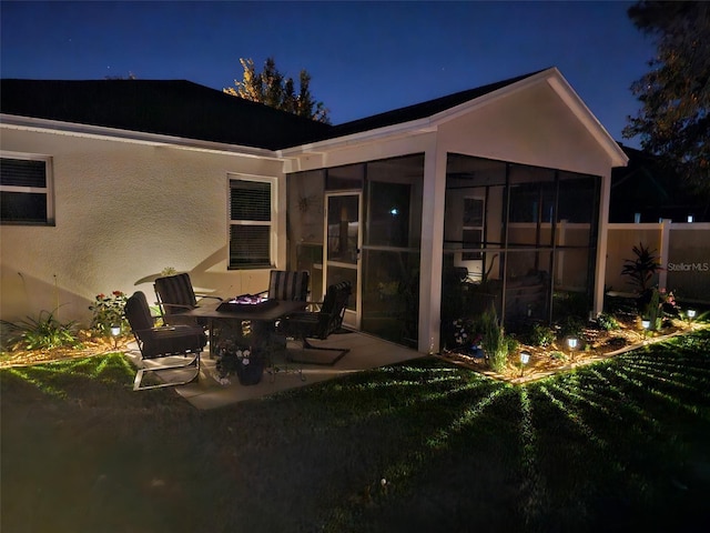 back of house at twilight featuring a lawn, fence, a sunroom, and stucco siding