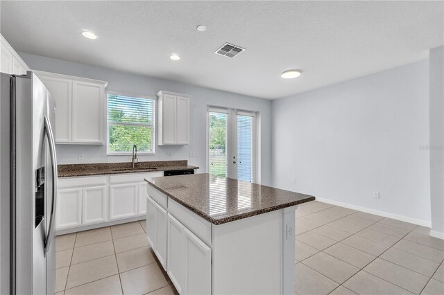 kitchen with white cabinets, a sink, stainless steel fridge with ice dispenser, a kitchen island, and visible vents