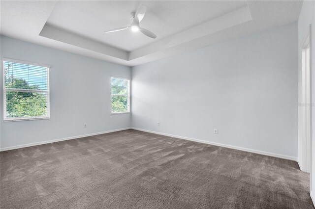 empty room with baseboards, a tray ceiling, ceiling fan, and dark colored carpet