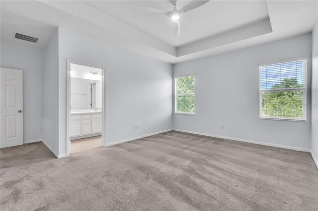 unfurnished bedroom with visible vents, a raised ceiling, baseboards, carpet flooring, and ensuite bath