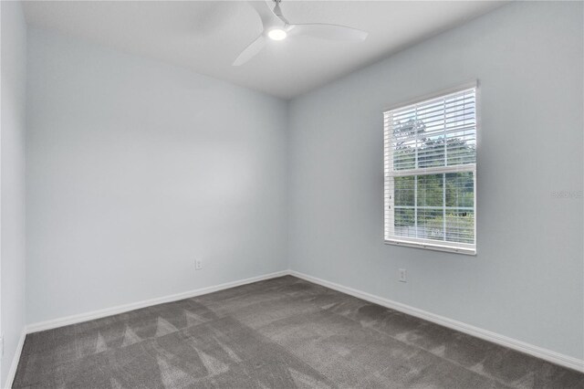 spare room with a ceiling fan, baseboards, and dark colored carpet