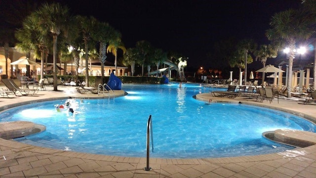 pool at twilight featuring a water slide, a patio, and a community pool