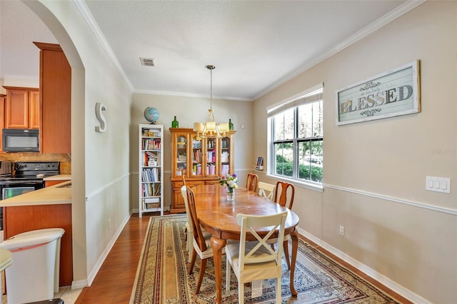 dining area with visible vents, arched walkways, wood finished floors, an inviting chandelier, and ornamental molding