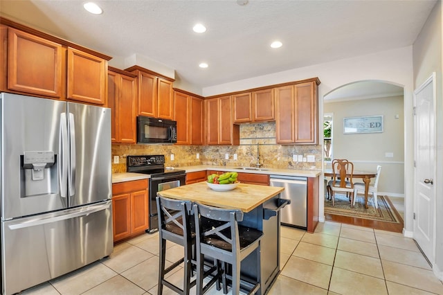 kitchen with a sink, arched walkways, decorative backsplash, light tile patterned floors, and black appliances