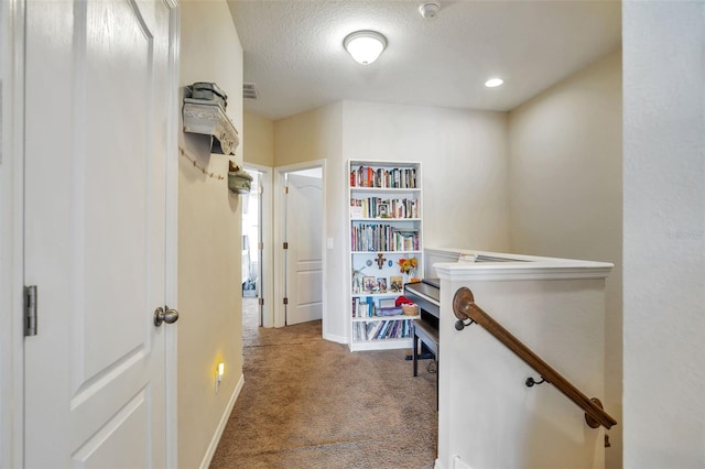 hallway with carpet floors, a textured ceiling, baseboards, an upstairs landing, and visible vents