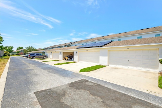 view of front of property featuring roof mounted solar panels, stucco siding, a residential view, and concrete driveway
