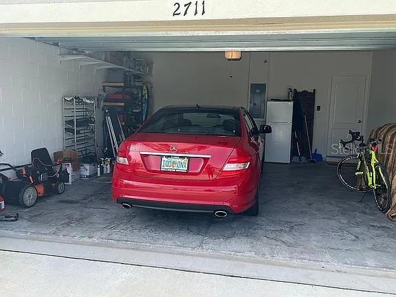2711 Neverland Dr, New Smyrna Beach, FL 32168 - garage with freestanding refrigerator, electric panel, concrete block wall, and a garage door opener