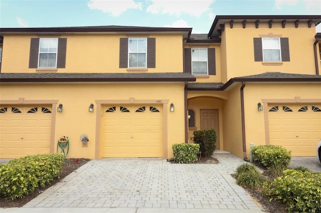 view of property featuring stucco siding, decorative driveway, and a garage