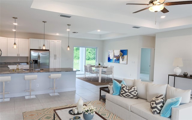 living room with light tile patterned floors, a tray ceiling, visible vents, and ceiling fan