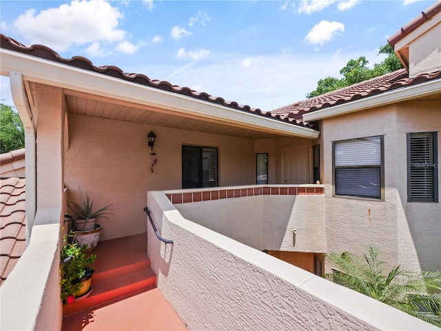 entrance to property with a tile roof, a balcony, and stucco siding