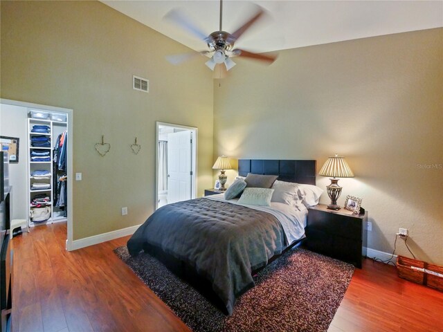 bedroom with a high ceiling, a walk in closet, baseboards, wood finished floors, and visible vents