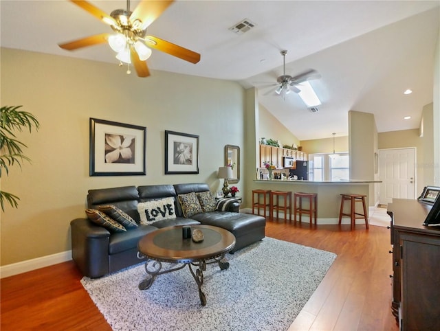 living room featuring visible vents, lofted ceiling, wood finished floors, baseboards, and a ceiling fan