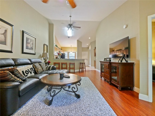living area featuring vaulted ceiling, baseboards, a ceiling fan, and wood finished floors