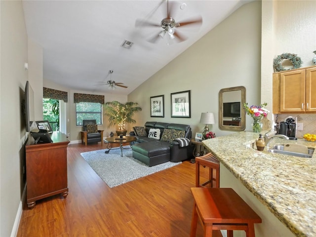 living room with visible vents, baseboards, high vaulted ceiling, a ceiling fan, and light wood-style flooring