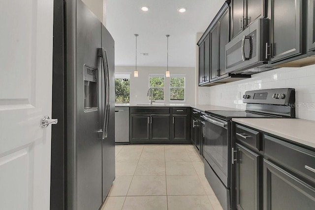 kitchen with backsplash, light countertops, a sink, appliances with stainless steel finishes, and light tile patterned floors
