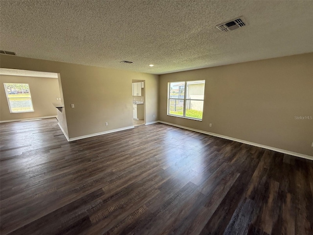 unfurnished room with baseboards, dark wood-style floors, a textured ceiling, and visible vents