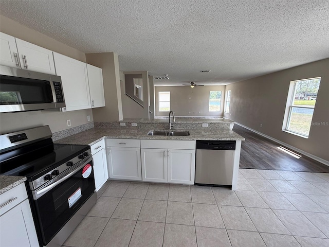 kitchen featuring a peninsula, open floor plan, a textured ceiling, a sink, and appliances with stainless steel finishes