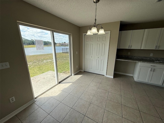 unfurnished dining area with light tile patterned flooring, a notable chandelier, a textured ceiling, baseboards, and a water view