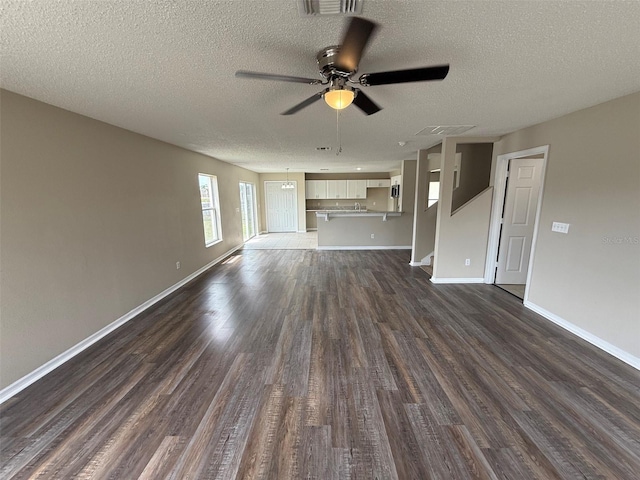 unfurnished living room with a textured ceiling, ceiling fan, dark wood finished floors, and baseboards