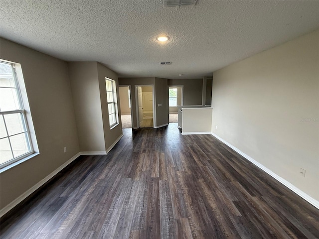 interior space featuring baseboards, dark wood-style floors, a textured ceiling, and visible vents