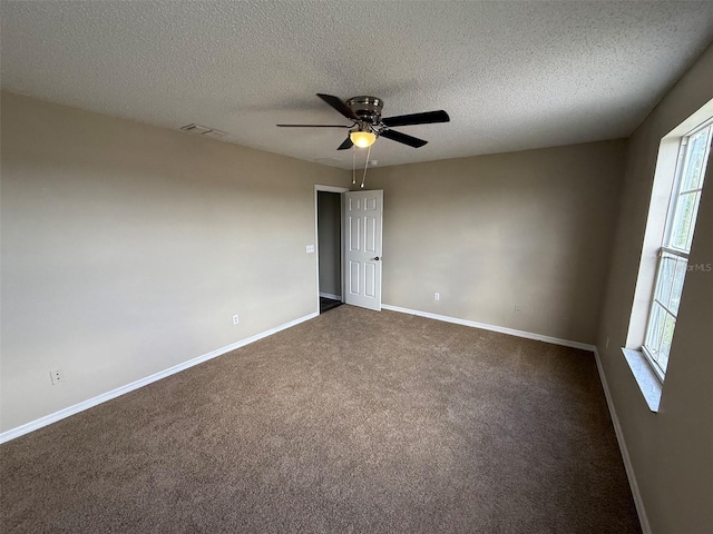 empty room with ceiling fan, a textured ceiling, dark colored carpet, baseboards, and visible vents
