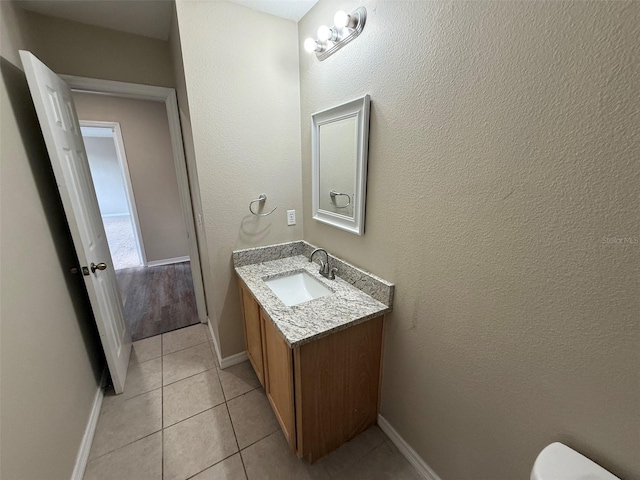 half bathroom with toilet, baseboards, tile patterned flooring, and vanity