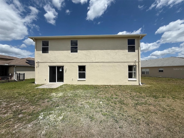 rear view of property with a lawn, fence, and stucco siding