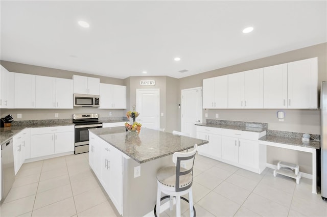 kitchen featuring a breakfast bar area, a kitchen island, light stone counters, white cabinets, and stainless steel appliances