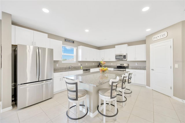 kitchen with a kitchen bar, a center island, a sink, white cabinets, and stainless steel appliances