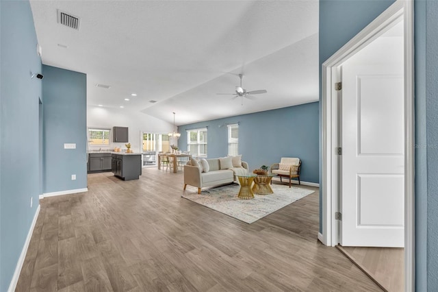1397 Gatlin Pl, The Villages, FL 32163 - living area featuring baseboards, vaulted ceiling, light wood finished floors, and ceiling fan with notable chandelier