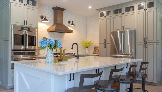kitchen featuring wall chimney range hood, a kitchen breakfast bar, tasteful backsplash, a center island with sink, and recessed lighting