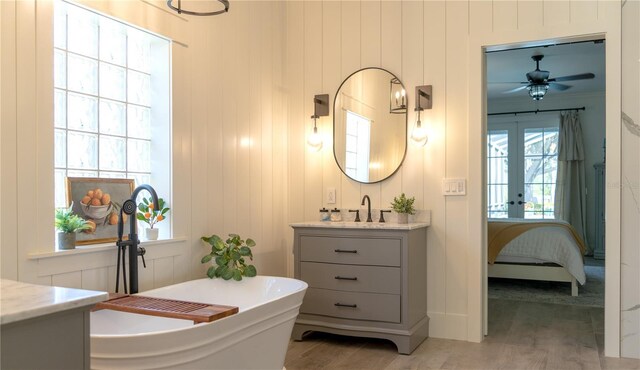bathroom with french doors, wood finished floors, vanity, a soaking tub, and ensuite bath