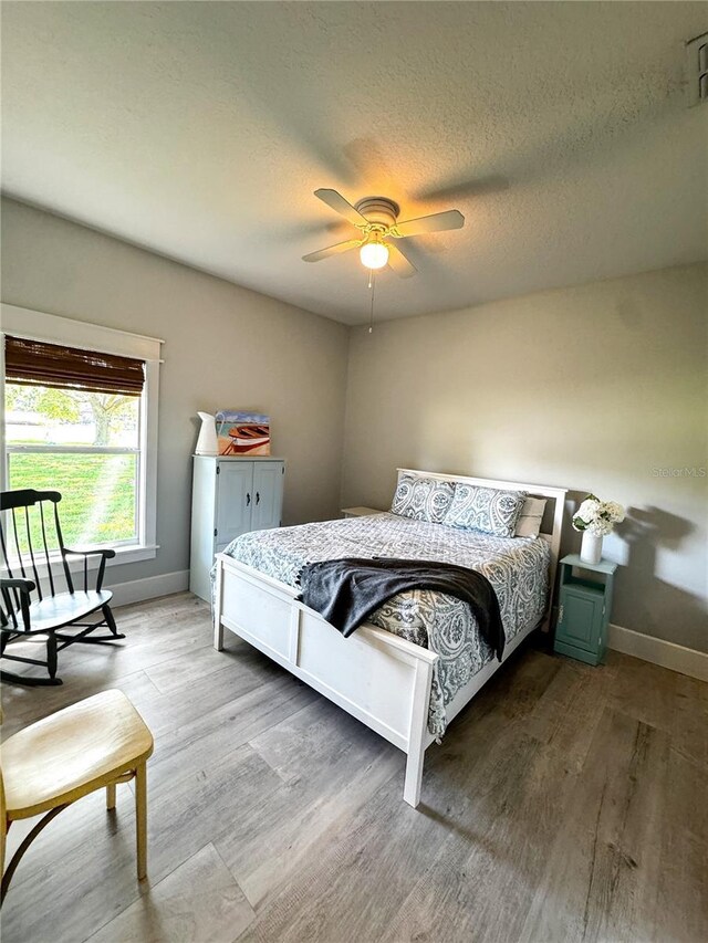 bedroom with baseboards, a textured ceiling, ceiling fan, and wood finished floors
