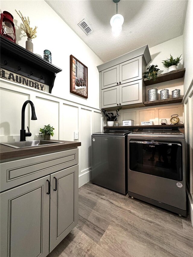 laundry area with visible vents, washing machine and clothes dryer, cabinet space, a sink, and light wood finished floors