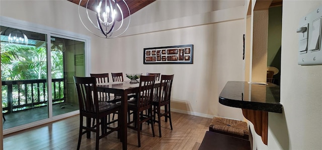 dining space with baseboards, lofted ceiling, wood finished floors, and a notable chandelier